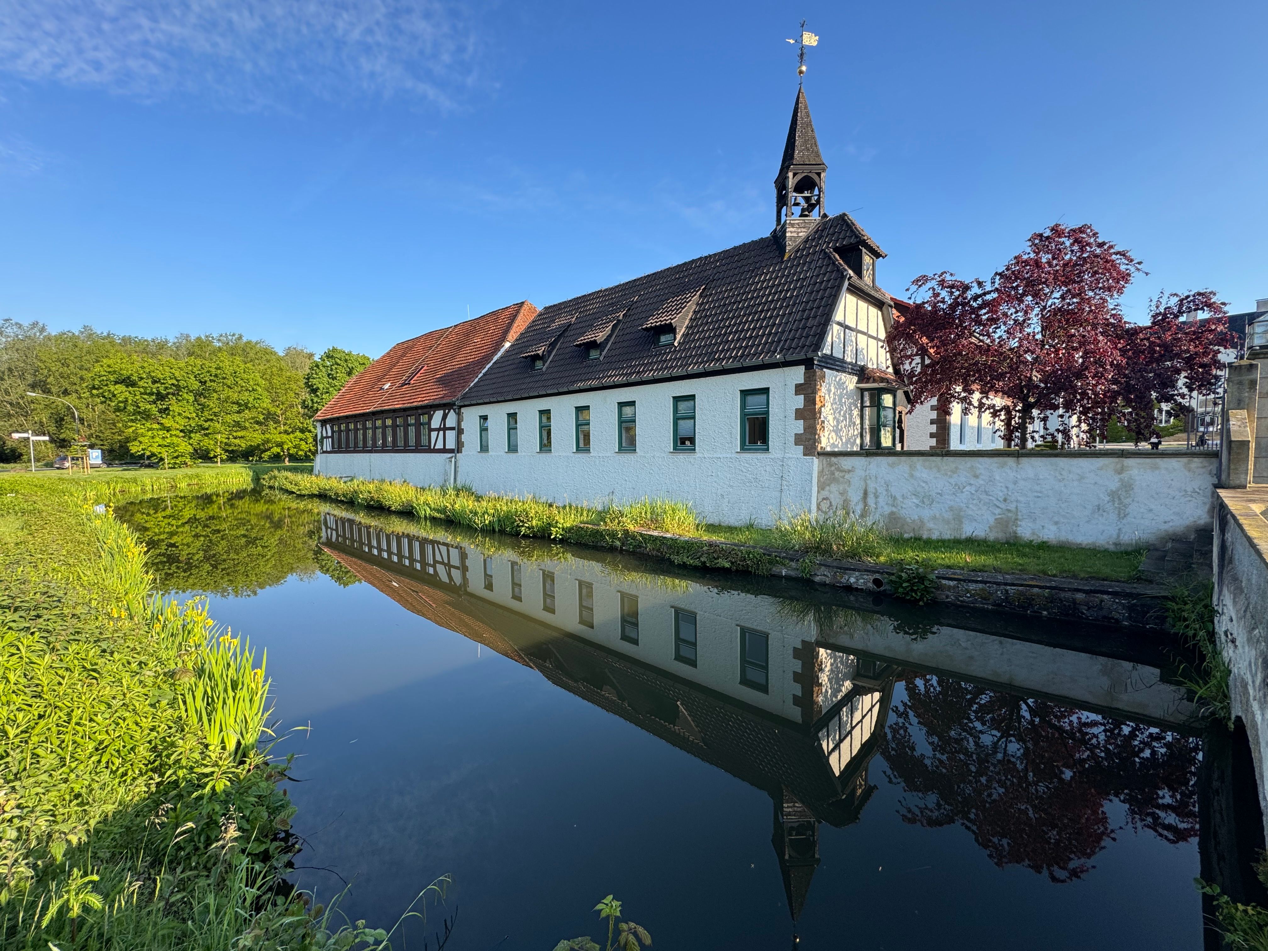 Historisches Gebäude mit Spiegelung im Wassergraben bei klarem Himmel - Symbol für Ruhe, Fokus und strukturiertes Arbeiten im Workshop.
